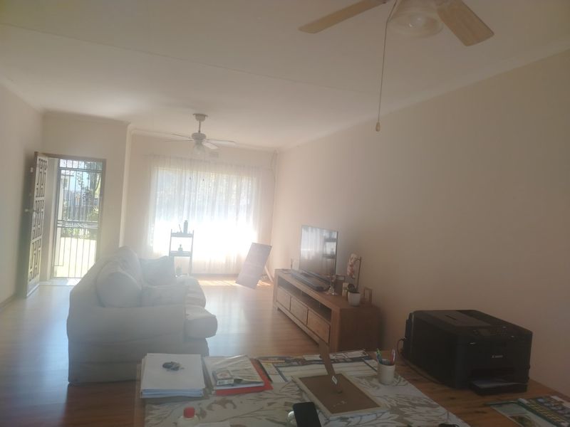 A spacious living room featuring laminate flooring, ceiling fans, and direct access to the exterior through a security gate.