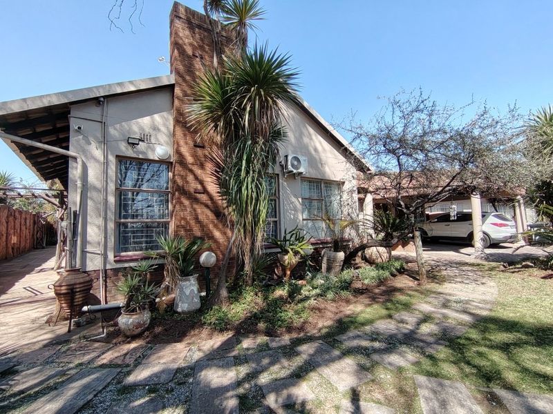 Rear view of the property featuring a brick chimney, established garden, paved pathways, and a covered carport area.