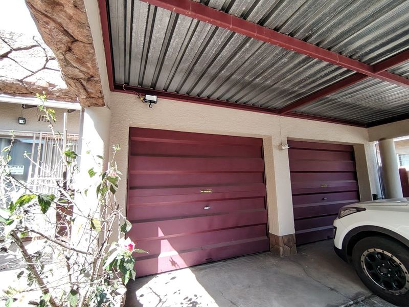 A double garage featuring red metal doors, corrugated roofing, and stone-clad pillars, providing secure covered parking.