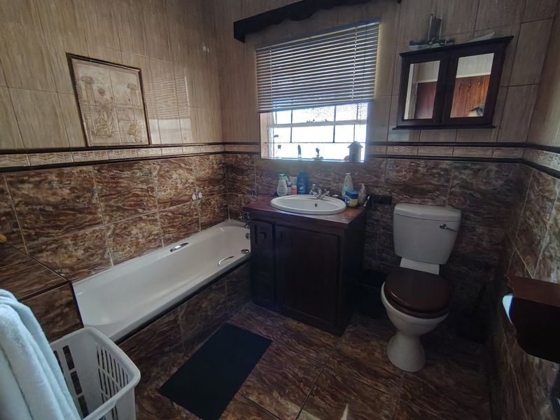 A functional bathroom featuring a built-in vanity, bathtub, and toilet, finished with dated floor-to-ceiling ceramic tiling.
