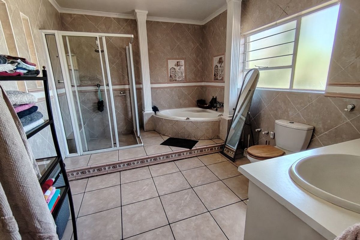 Spacious bathroom featuring a corner bathtub, separate shower enclosure, vanity sink, and toilet, finished with neutral wall and floor tiles.