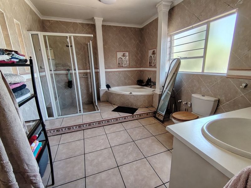 Spacious bathroom featuring a corner bathtub, separate shower enclosure, vanity sink, and toilet, finished with neutral wall and floor tiles.