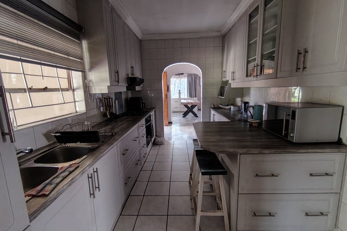 A functional galley-style kitchen featuring ample built-in cabinetry, laminate countertops, a double sink, and tiled flooring, leading through an archway to the dining area.