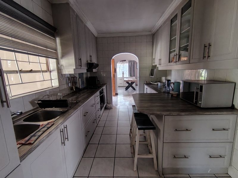 A functional galley-style kitchen featuring ample built-in cabinetry, laminate countertops, a double sink, and tiled flooring, leading through an archway to the dining area.