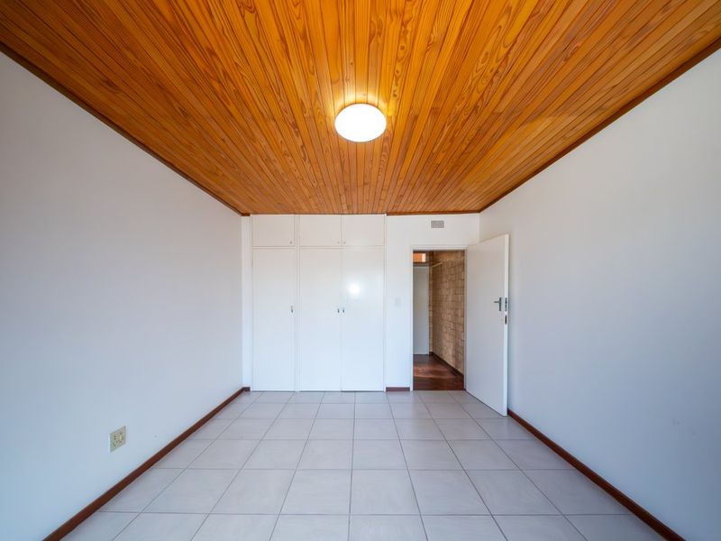 An empty bedroom featuring tiled flooring, built-in cupboards, and a distinctive timber-paneled ceiling.