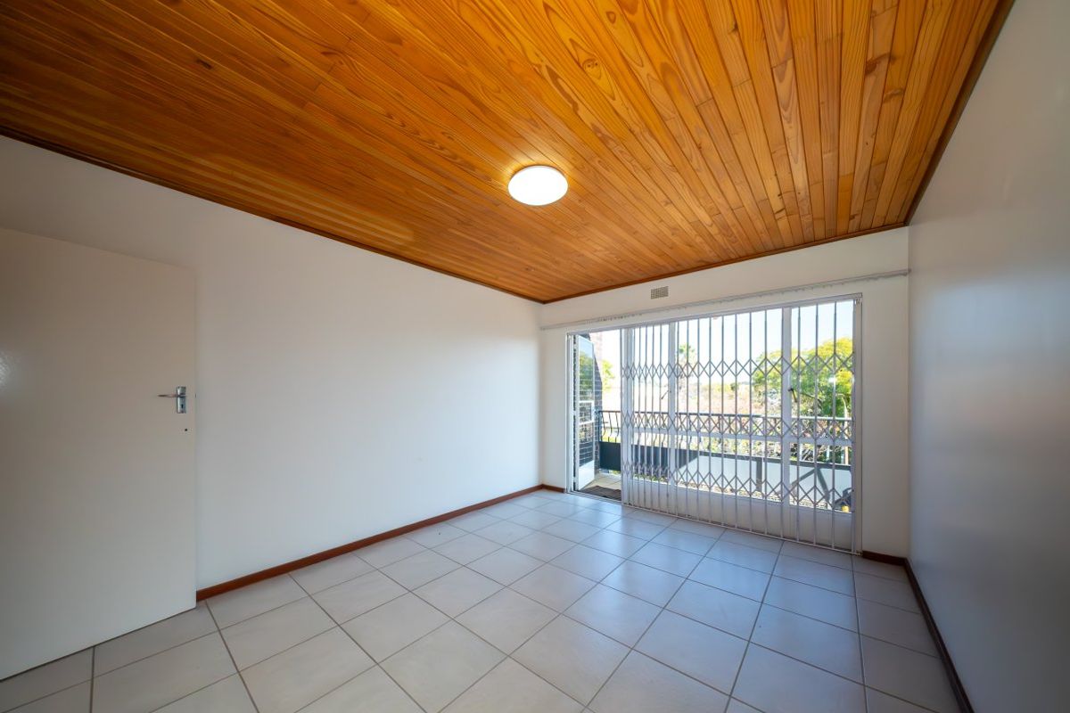 An empty bedroom featuring tiled flooring, a timber-paneled ceiling, and a sliding glass door with a security gate leading to a balcony.
