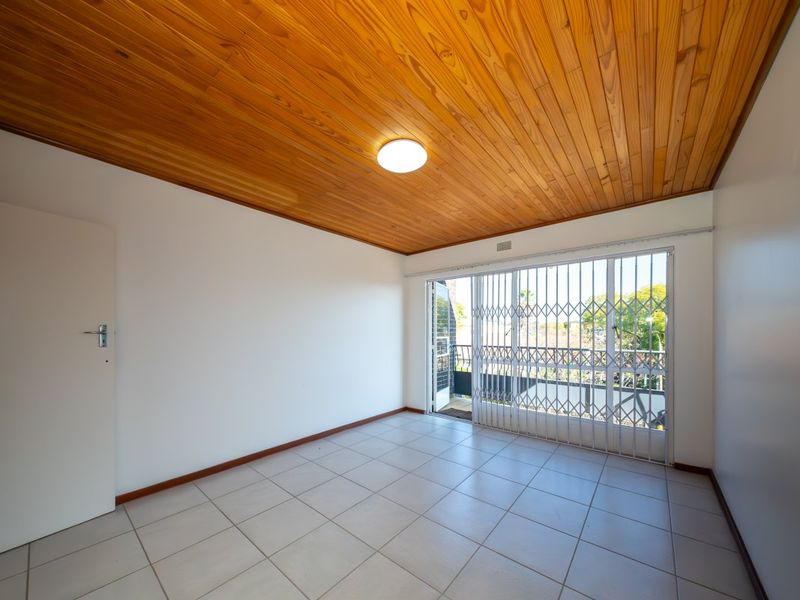 An empty bedroom featuring tiled flooring, a timber-paneled ceiling, and a sliding glass door with a security gate leading to a balcony.
