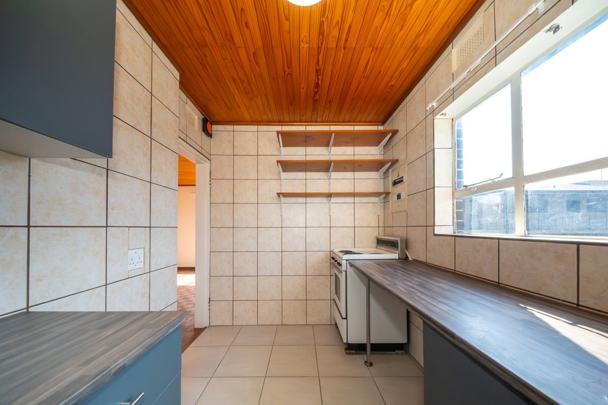 A functional kitchen featuring tiled walls, timber ceiling, laminate countertops, and a freestanding stove with open shelving for storage.