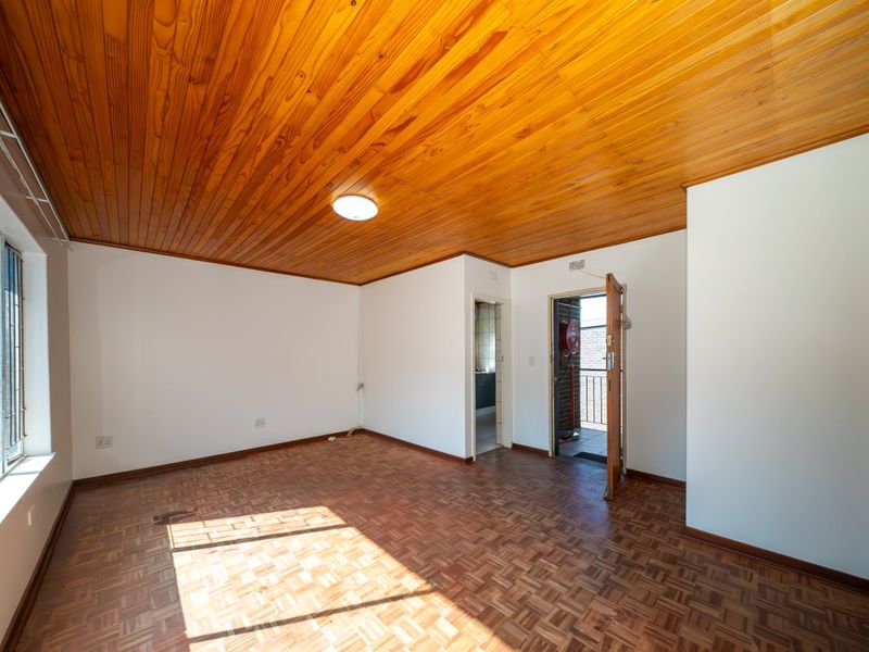 An empty living room featuring classic wooden parquet flooring and a warm timber tongue and groove ceiling, offering a blank canvas for interior design.
