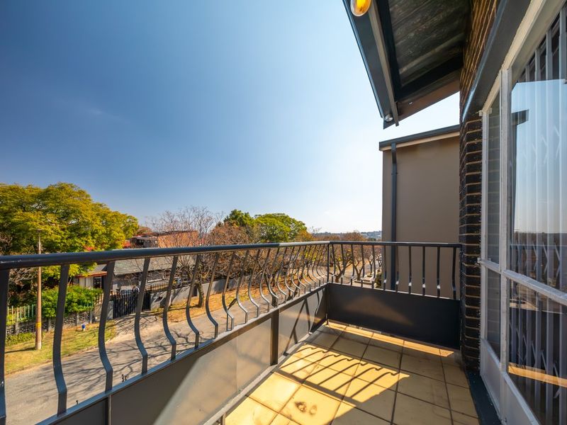 A private balcony featuring tiled flooring and a metal balustrade, offering an elevated view of the surrounding neighborhood.