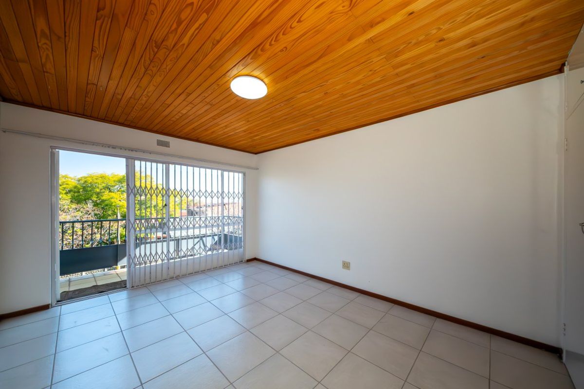 Empty bedroom featuring ceramic floor tiles, a wooden tongue and groove ceiling, and a sliding glass door with a security gate leading to a balcony.