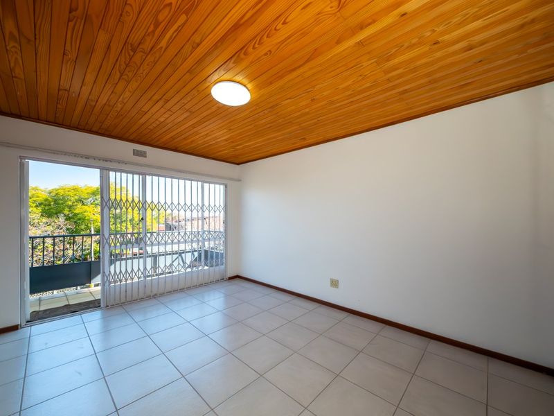 Empty bedroom featuring ceramic floor tiles, a wooden tongue and groove ceiling, and a sliding glass door with a security gate leading to a balcony.