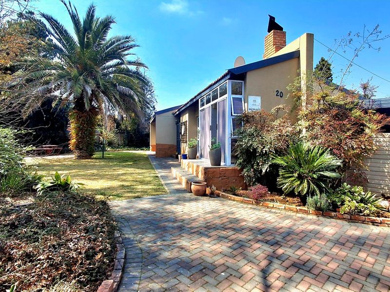 Front view of the property featuring a brick paved driveway, established garden with mature palm tree, and a brick chimney stack.