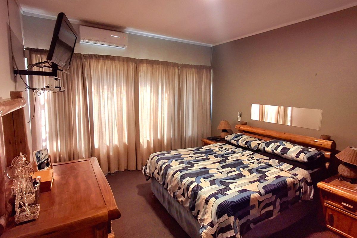 A functional bedroom featuring a wall-mounted air conditioning unit, curtained window, and integrated wall mirror, providing a comfortable and practical sleeping space.