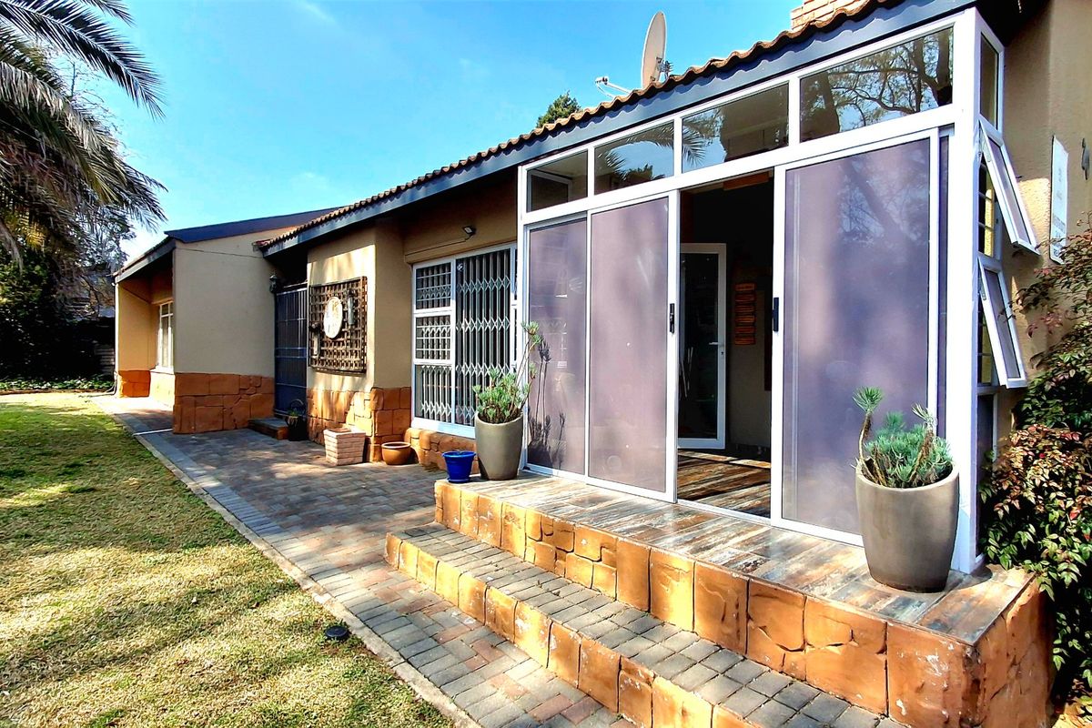 Rear exterior view featuring a paved patio area, sliding glass doors with security gates, and brick-clad wall finishes overlooking a garden.