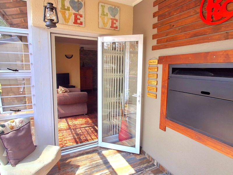 Covered patio area featuring a built-in braai, timber wall accents, tiled flooring, and direct access to the interior living space through an aluminium door.