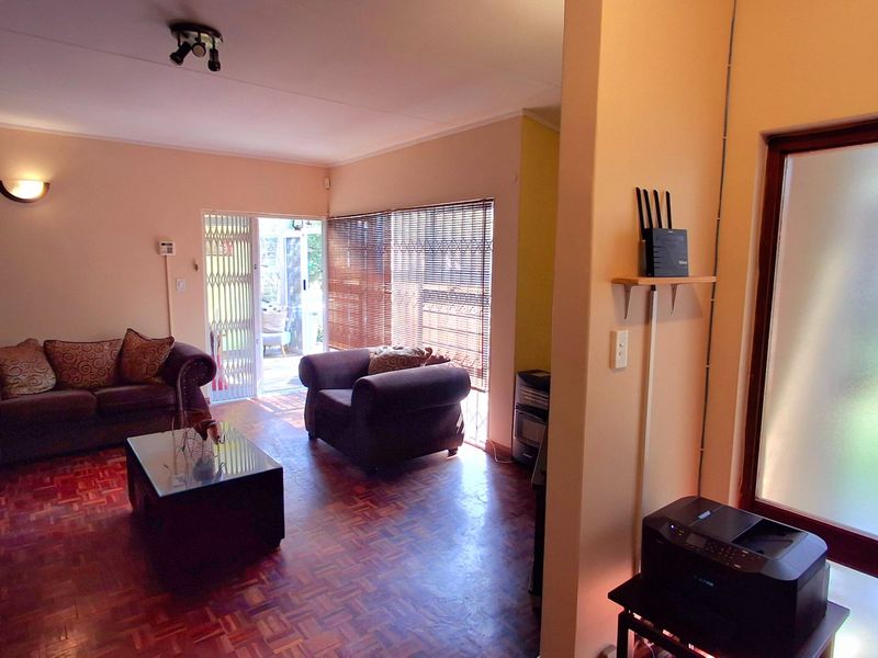 A living room featuring classic parquet flooring, a security gate leading to the patio, and a frosted glass entrance door.