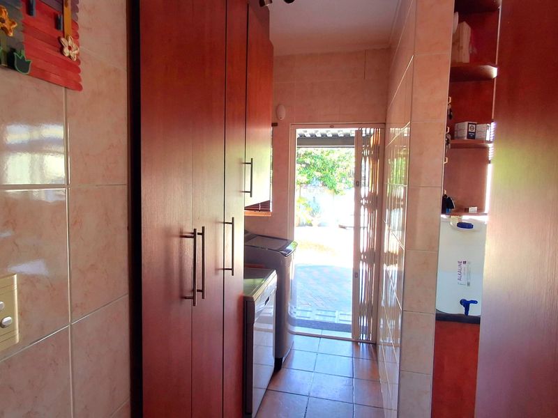 A functional laundry area featuring built-in cabinetry, tiled finishes, and direct access to the exterior through a security gate.