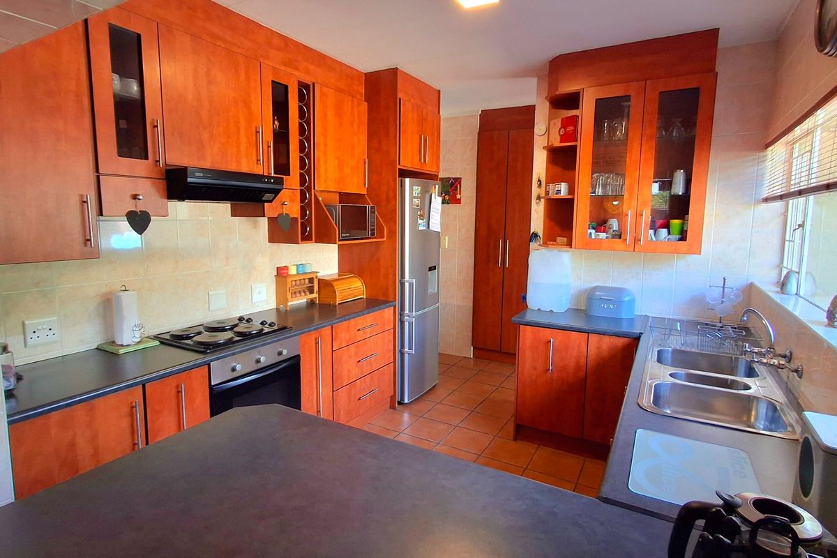 A functional kitchen featuring warm-toned wooden cabinetry, dark laminate countertops, a built-in oven and hob, and a double stainless steel sink.