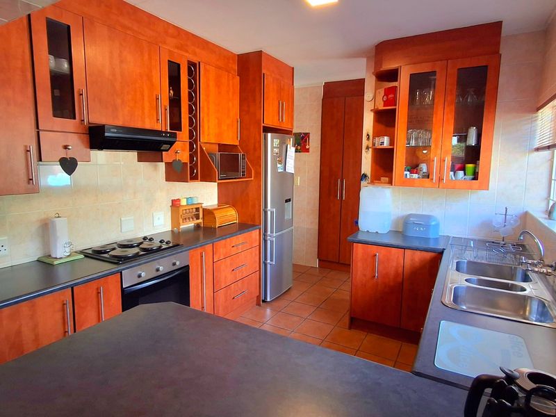 A functional kitchen featuring warm-toned wooden cabinetry, dark laminate countertops, a built-in oven and hob, and a double stainless steel sink.