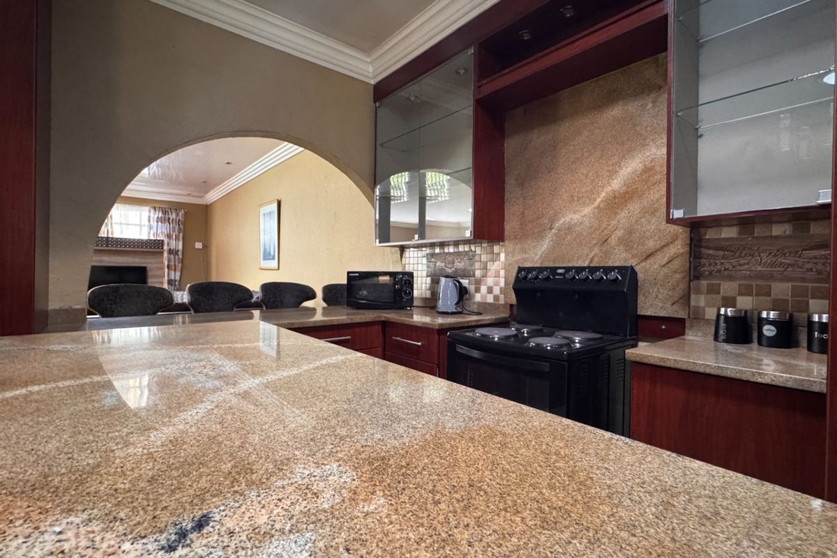 A kitchen featuring granite countertops, dark wood cabinetry, and a stone tile backsplash, connected to the living area via a decorative archway.
