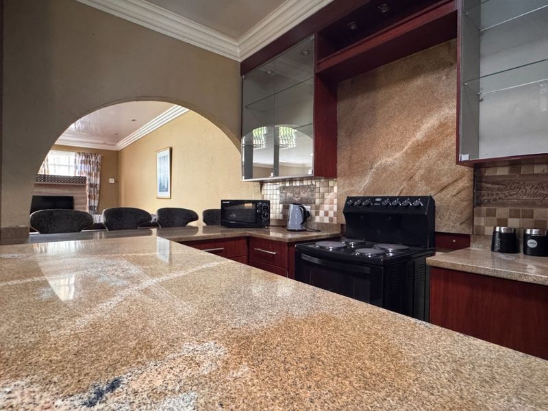 A kitchen featuring granite countertops, dark wood cabinetry, and a stone tile backsplash, connected to the living area via a decorative archway.