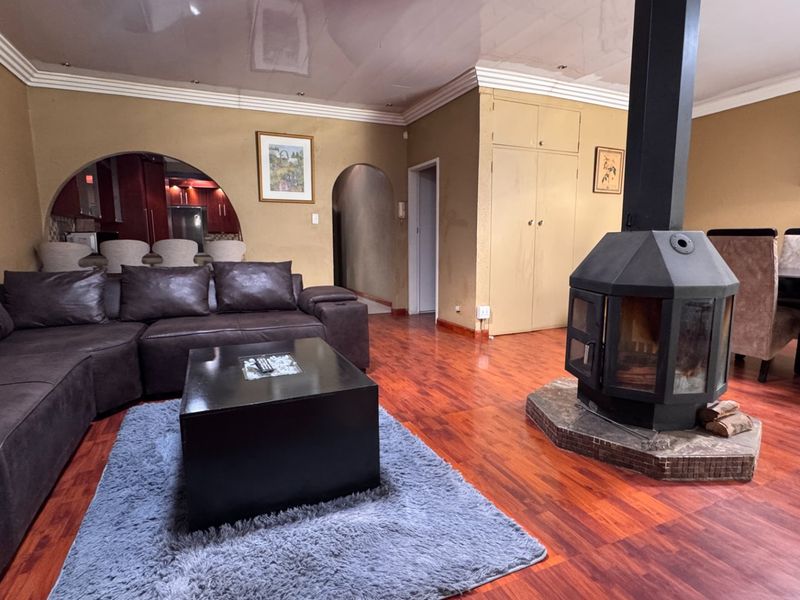 Spacious open-plan living area featuring a central freestanding fireplace, laminate flooring, and an arched transition to the kitchen area.