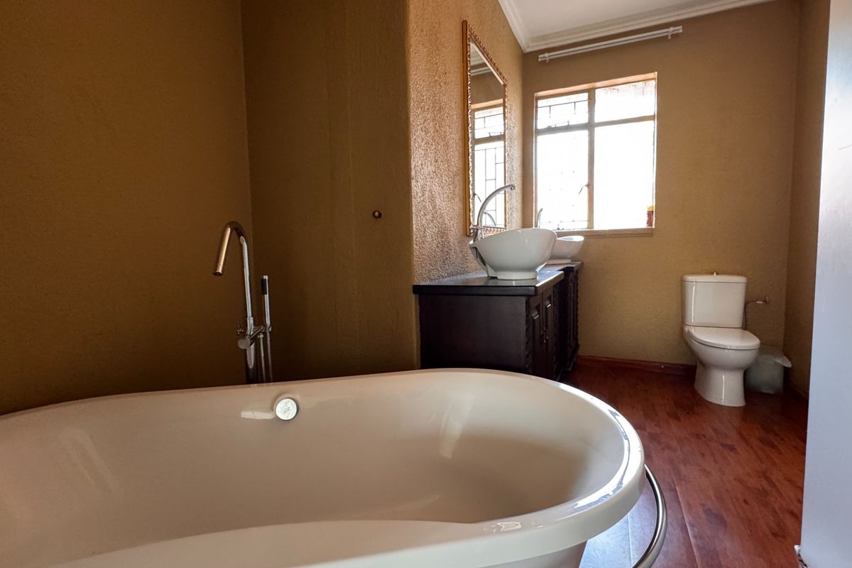A bathroom featuring a freestanding bathtub, floor-mounted faucet, vanity with vessel sink, and a toilet, finished with warm-toned walls and wood-look flooring.