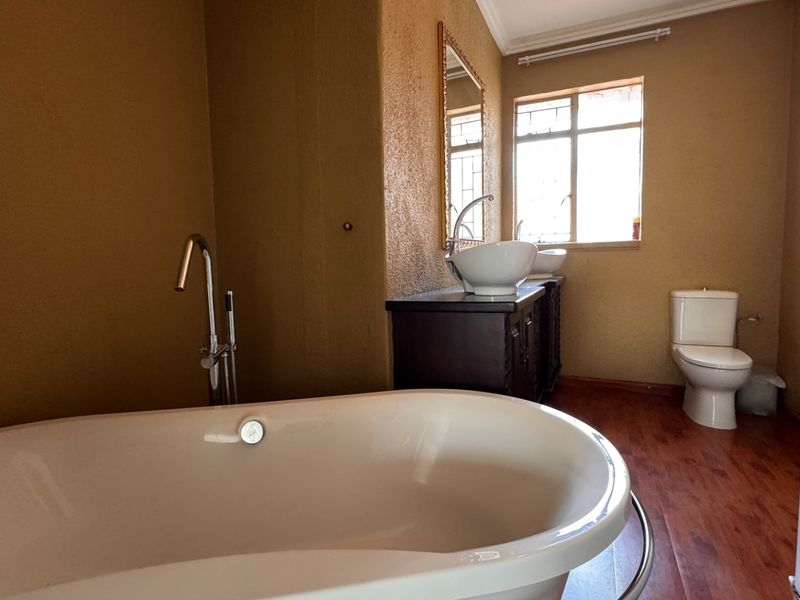 A bathroom featuring a freestanding bathtub, floor-mounted faucet, vanity with vessel sink, and a toilet, finished with warm-toned walls and wood-look flooring.