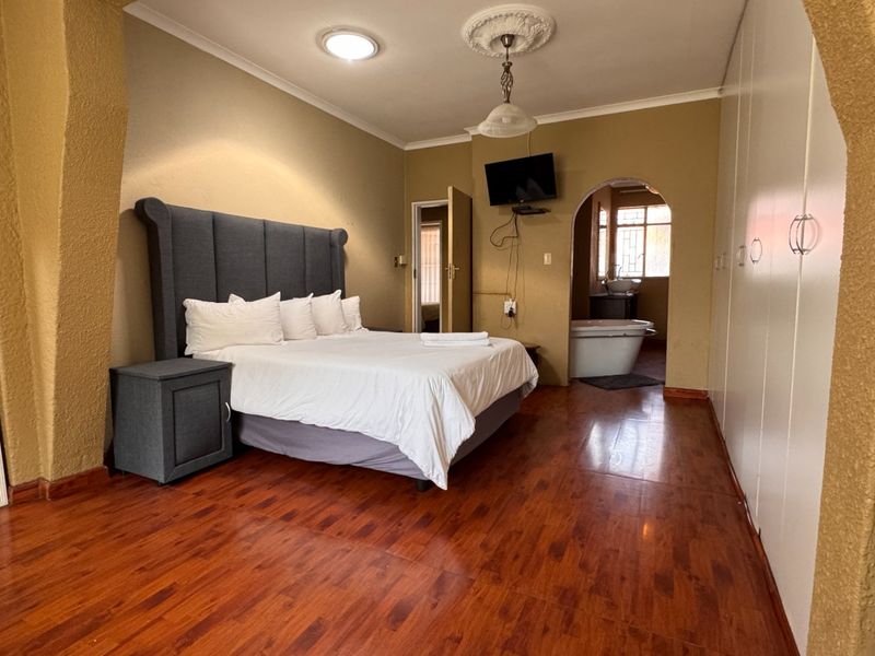 Spacious bedroom featuring laminate flooring, built-in cupboards, and an open archway leading to an en-suite bathroom area.