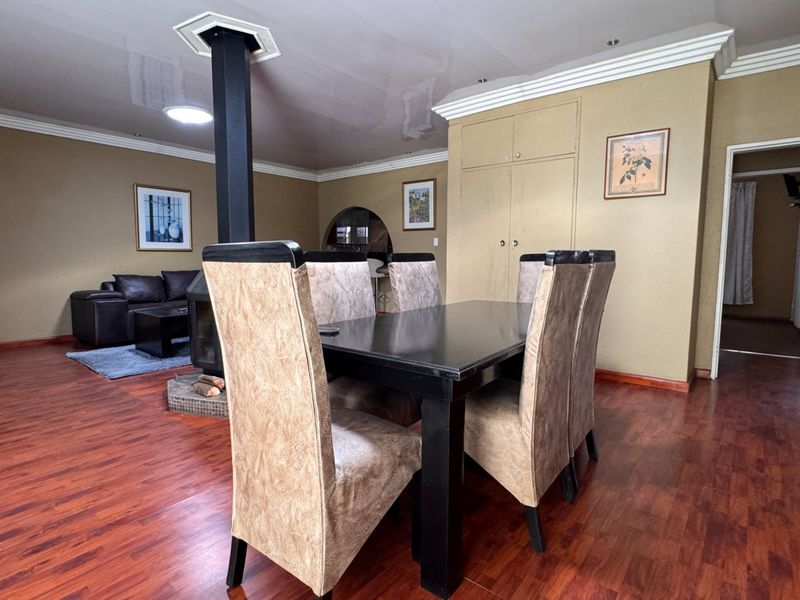 Spacious open-plan living and dining area featuring laminate flooring, a central freestanding fireplace, and built-in storage cupboards.