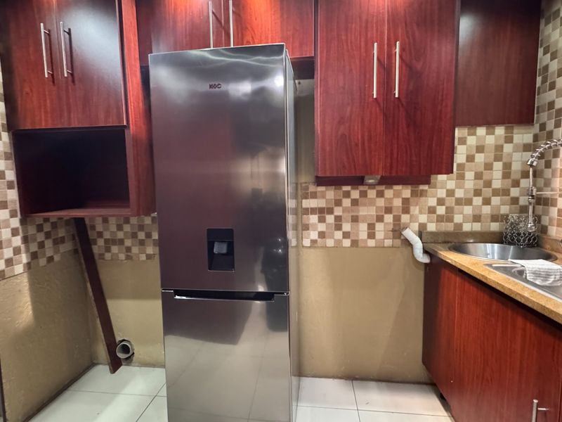 A kitchen area featuring dark wood-finish cabinetry, a stainless steel sink with a gooseneck faucet, and a tiled backsplash, requiring minor repairs.