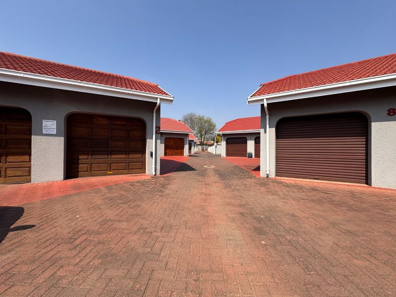 A view of a paved driveway leading between multiple garage units with tiled roofs and various garage door styles in a townhouse complex.