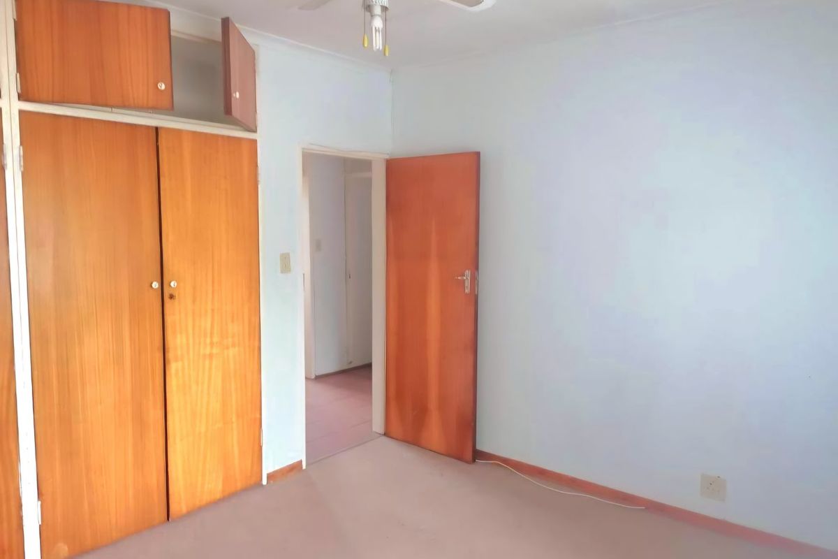 An empty bedroom featuring built-in wooden cupboards, a ceiling fan, and carpeted flooring, offering a blank canvas for renovation.