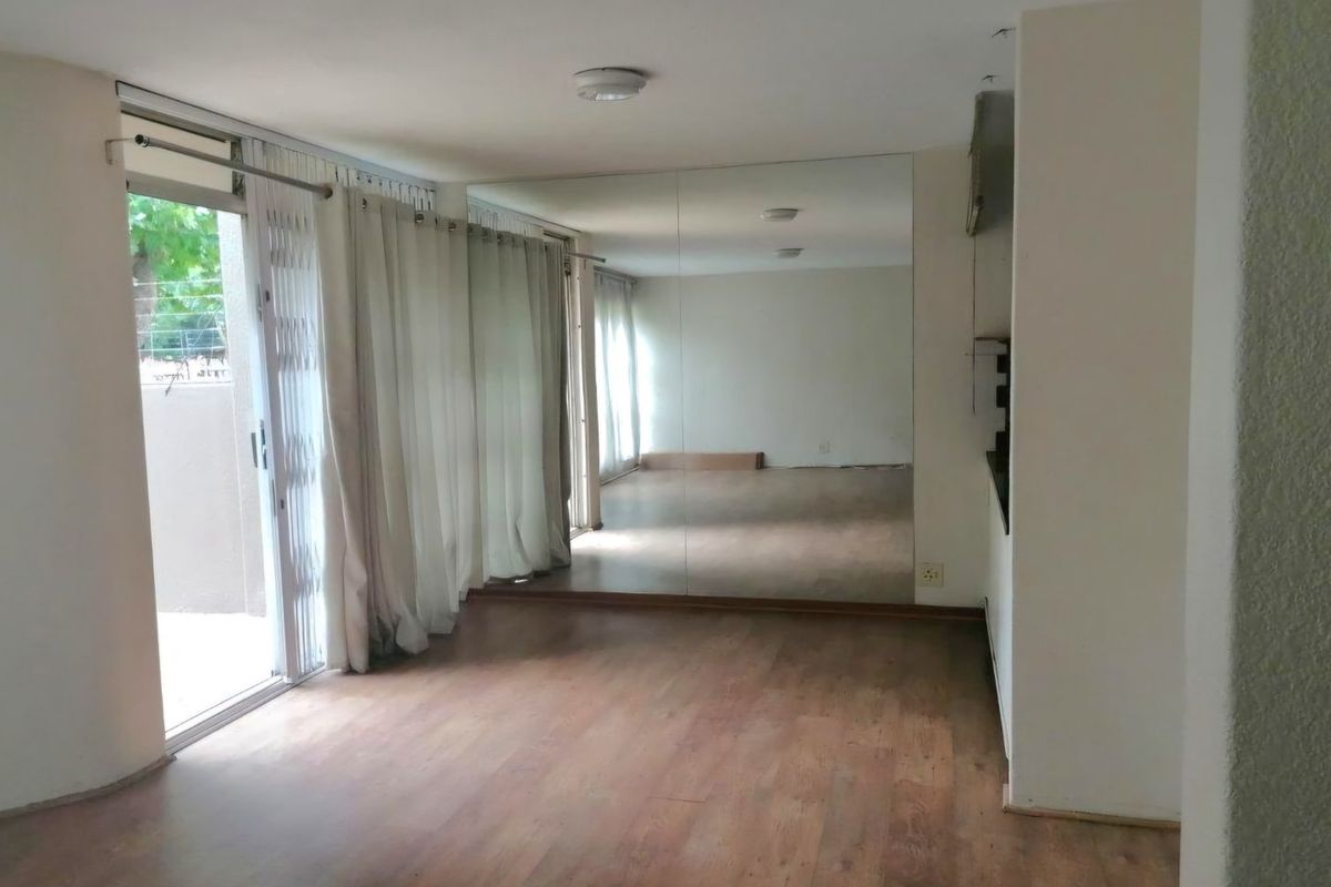 An empty living area featuring laminate flooring, a large wall-to-wall mirror, and a sliding glass door providing access to the outdoor space.