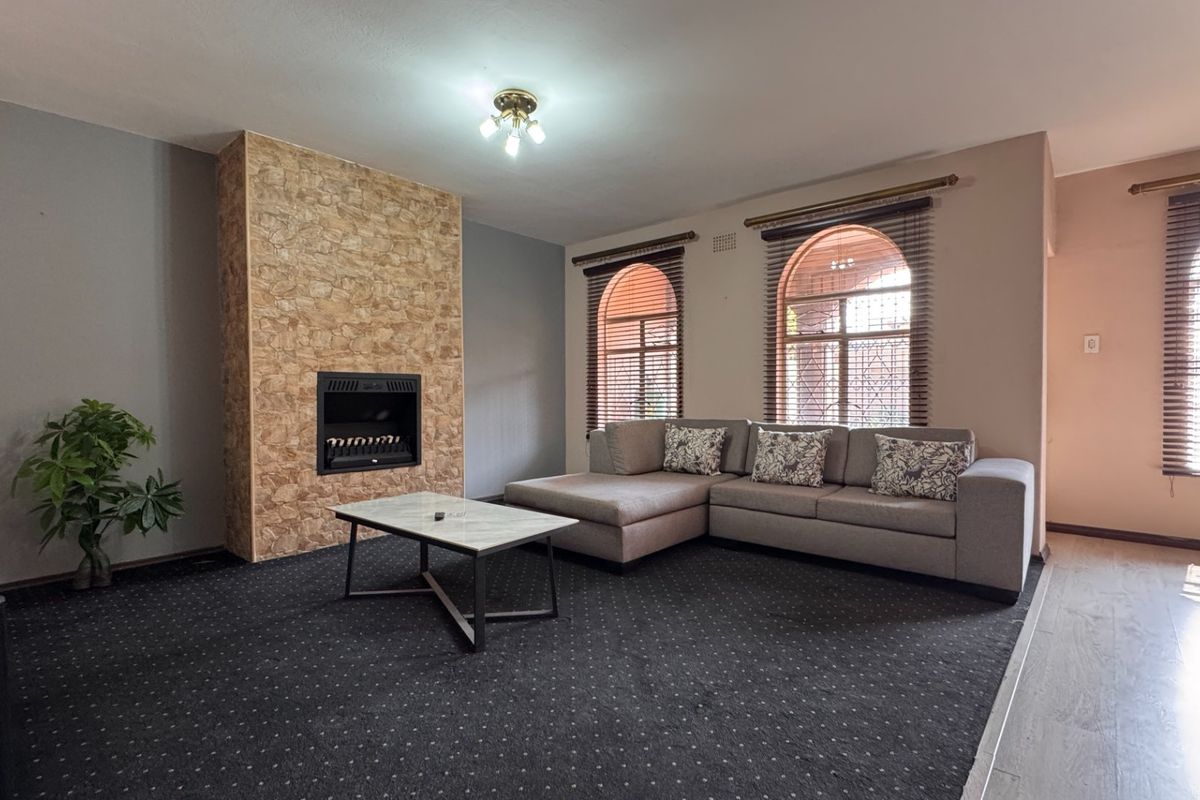 Spacious living room featuring a stone-clad built-in fireplace and distinctive arched windows with fitted blinds, offering a comfortable and well-defined lounge area.