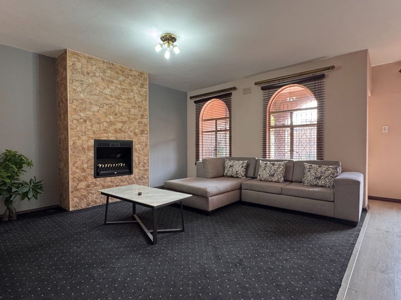 Spacious living room featuring a stone-clad built-in fireplace and distinctive arched windows with fitted blinds, offering a comfortable and well-defined lounge area.