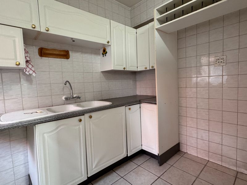 A dated kitchen featuring white built-in cabinetry, tiled splashbacks, and a double basin sink, offering a blank canvas for renovation.