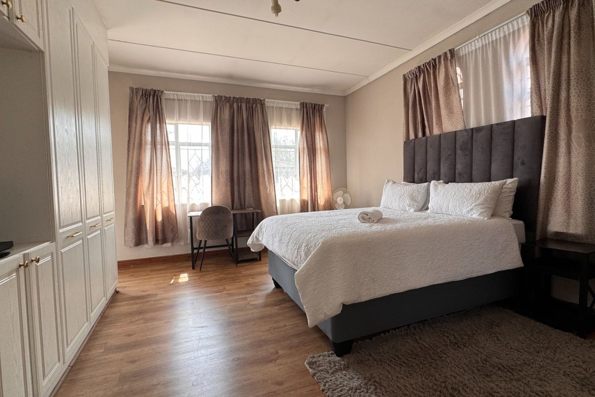 A well-maintained bedroom featuring laminate flooring, built-in cupboards, and large windows that provide ample natural light.