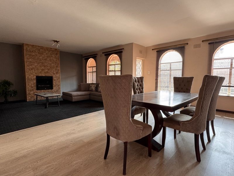 Spacious open-plan living and dining area featuring a stone-clad fireplace, arched windows, and a combination of laminate and carpeted flooring.
