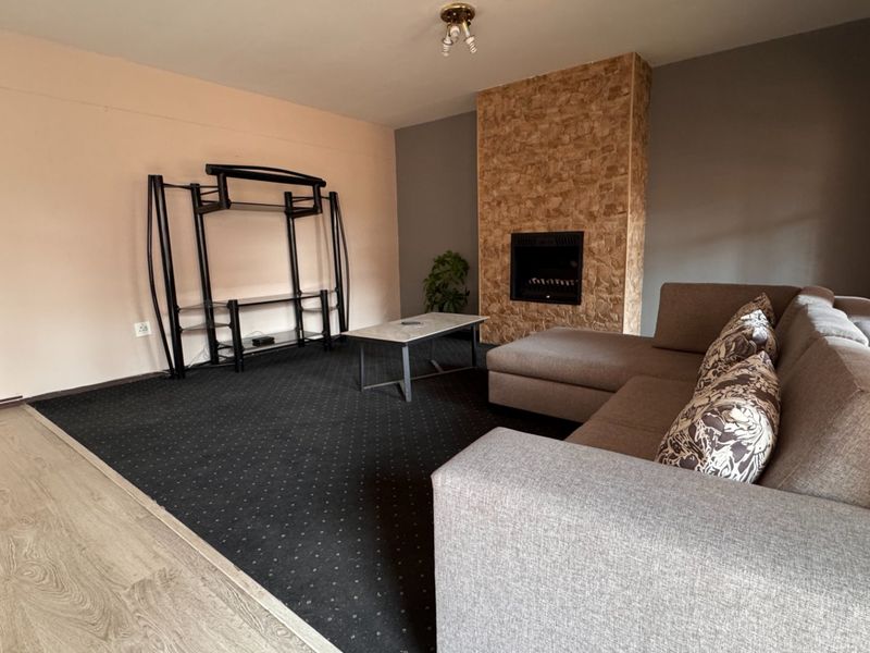 A living room featuring a stone-clad built-in fireplace, dark carpeting, and wood-look flooring, offering a cozy space for relaxation.