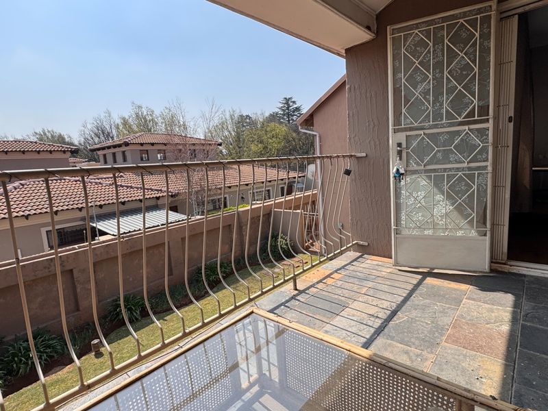 A private balcony featuring stone tile flooring, a metal balustrade, and a security gate, offering an elevated view of the surrounding residential complex.