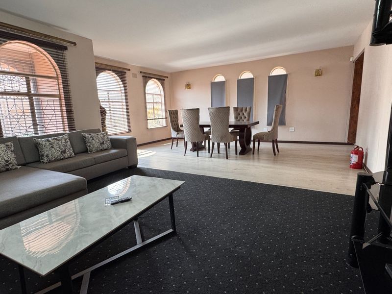 Spacious open-plan living and dining area featuring arched windows, a mix of carpet and laminate flooring, and wall-mounted lighting fixtures.