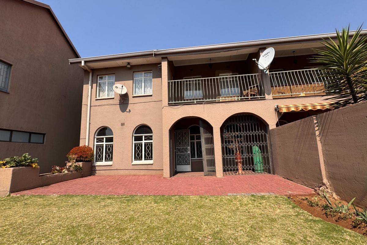 Rear view of the townhouse featuring a paved patio, a covered balcony, arched architectural details, and a private garden area.