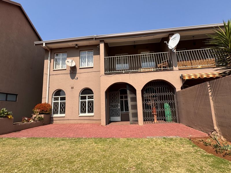 Rear view of the townhouse featuring a paved patio, a covered balcony, arched architectural details, and a private garden area.