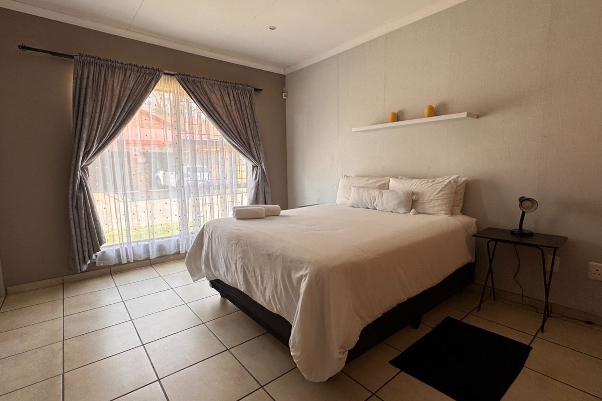 A functional bedroom featuring neutral wall tones, tiled flooring, and a large window with curtain rails, providing a clean and simple living space.