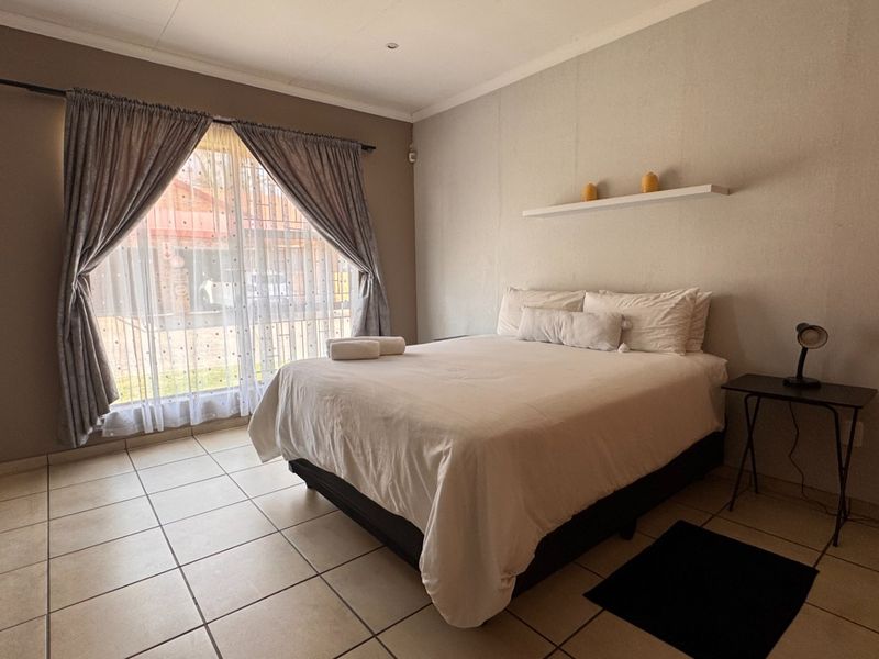 A functional bedroom featuring neutral wall tones, tiled flooring, and a large window with curtain rails, providing a clean and simple living space.