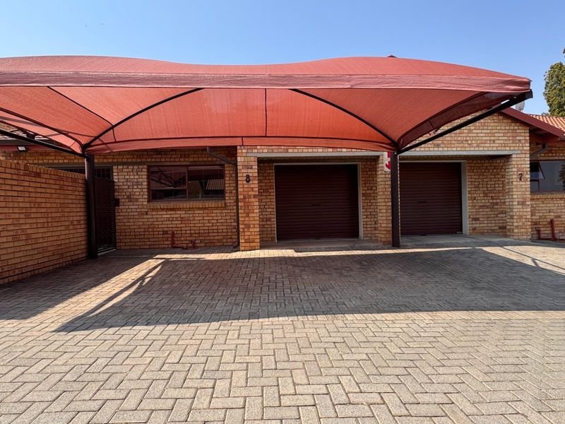 Front exterior view of a townhouse featuring a paved driveway, double garage, and a large red shade cloth carport structure.
