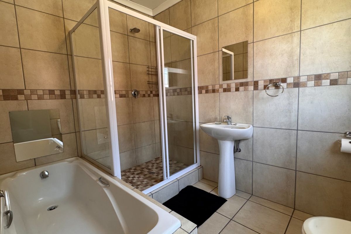 A functional bathroom featuring a shower enclosure, pedestal basin, and bathtub with neutral wall and floor tiling.