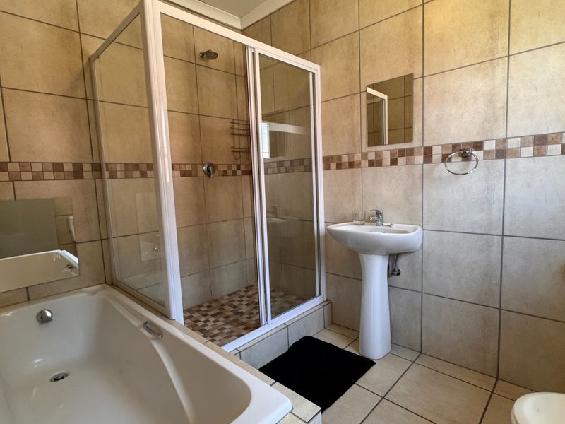 A functional bathroom featuring a shower enclosure, pedestal basin, and bathtub with neutral wall and floor tiling.